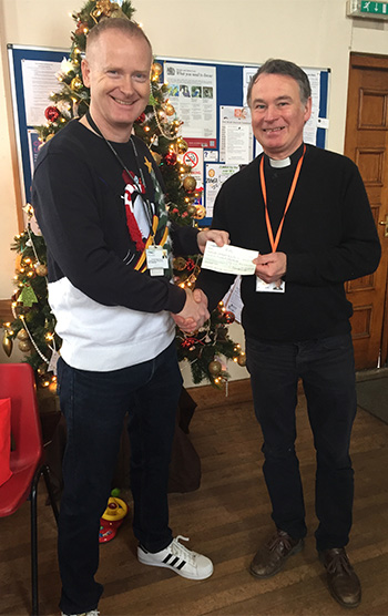 chairman handing a cheque over to a priest in front of a christmas tree